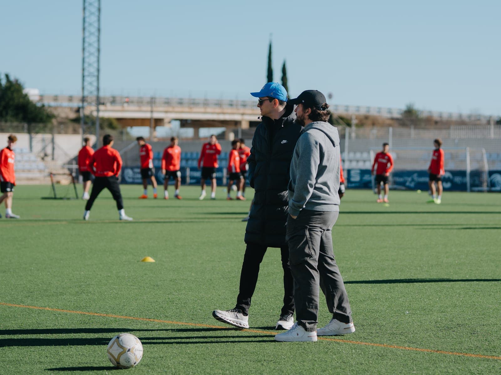 Dos entrenadores visitantes siguiendo una sesión del Eture FC desde el centro del campo