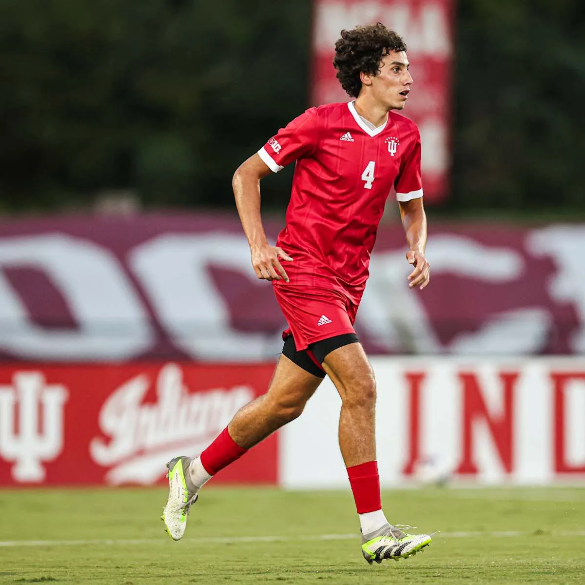 Hugo Bacharach runs on the pitch in a red Indiana University kit with the number 4, with Indiana banners behind him.